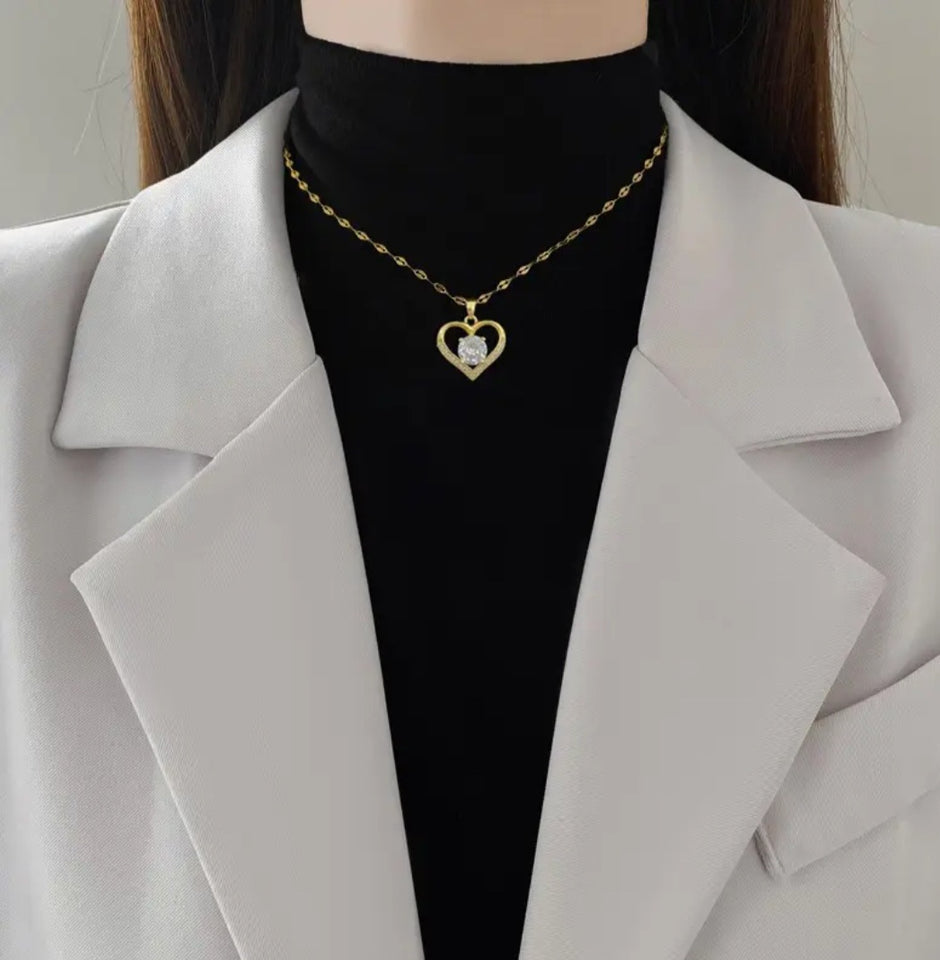 Sublimez votre tenue avec ce collier raffiné en acier inoxydable doré, conçu pour allier élégance et durabilité. Son pendentif en forme de cœur ajouré symbolise l’amour et la délicatesse, rehaussé d’une pierre centrale scintillante qui capte la lumière.