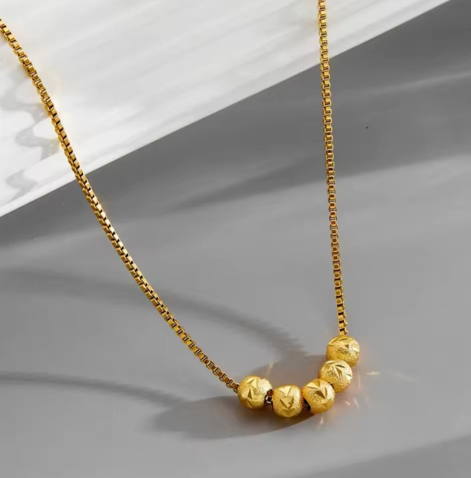 Collier en acier inoxydable doré, orné de cinq perles finement texturées. Un bijou délicat et lumineux, facile à porter au quotidien.