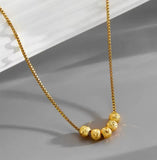 Collier en acier inoxydable doré, orné de cinq perles finement texturées. Un bijou délicat et lumineux, facile à porter au quotidien.