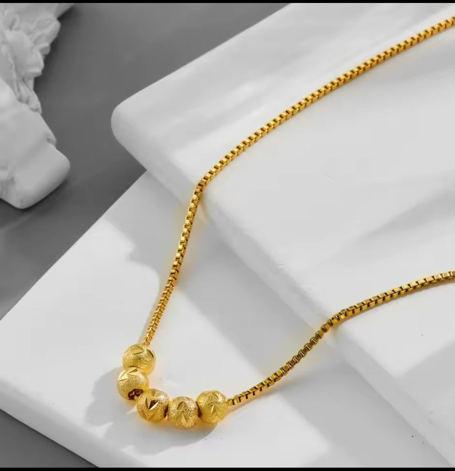 Collier en acier inoxydable doré, orné de cinq perles finement texturées. Un bijou délicat et lumineux, facile à porter au quotidien.