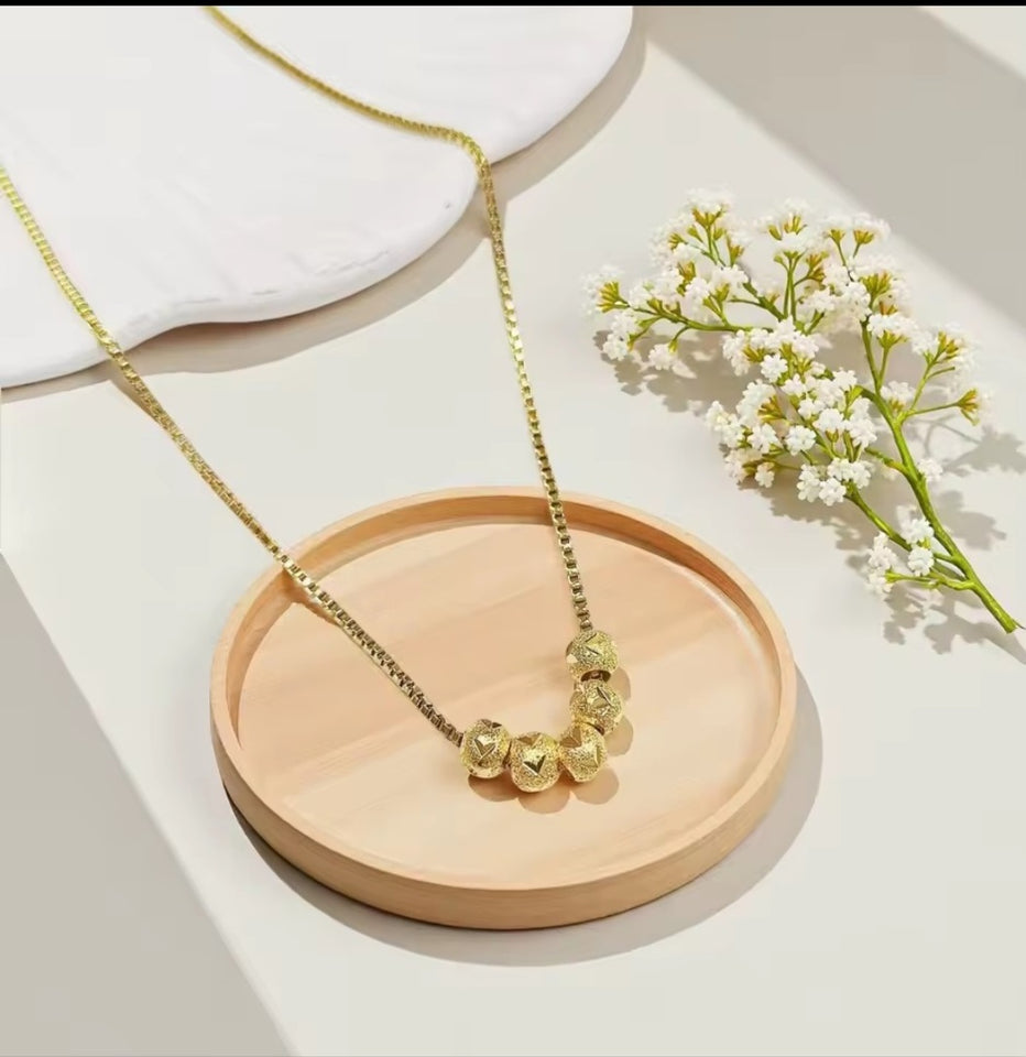 Collier en acier inoxydable doré, orné de cinq perles finement texturées. Un bijou délicat et lumineux, facile à porter au quotidien.