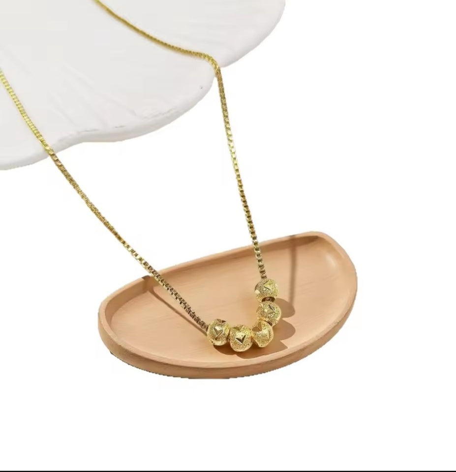 Collier en acier inoxydable doré, orné de cinq perles finement texturées. Un bijou délicat et lumineux, facile à porter au quotidien.